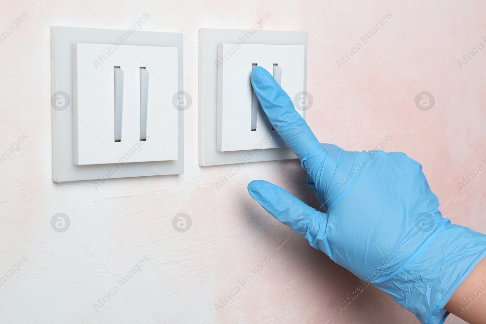 Photo of Woman in protective gloves pressing button of light switch indoors, closeup