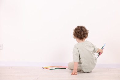 Photo of Little boy with colorful pencils near white wall indoors., back view. Space for text