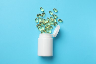 Photo of White bottle and different vitamin capsules on light blue background, top view