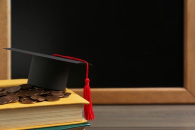 Photo of Scholarship concept. Graduation cap, books and coins on wooden table, space for text