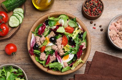 Photo of Bowl of delicious salad with canned tuna and ingredients on wooden table, flat lay