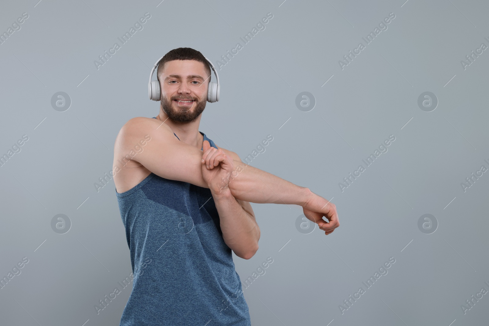 Photo of Handsome man with headphones stretching on grey background, space for text