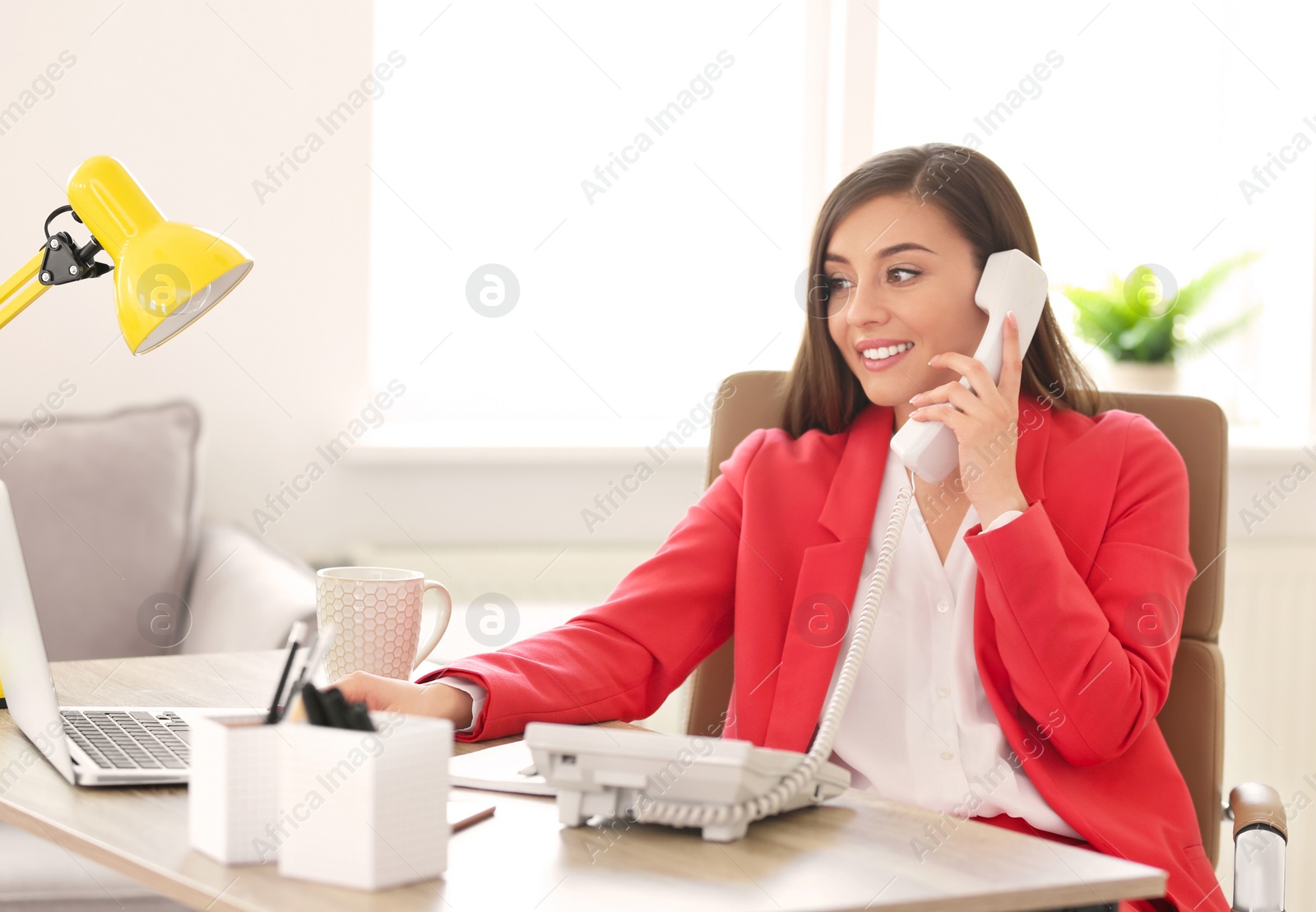 Photo of Young woman talking on phone at workplace