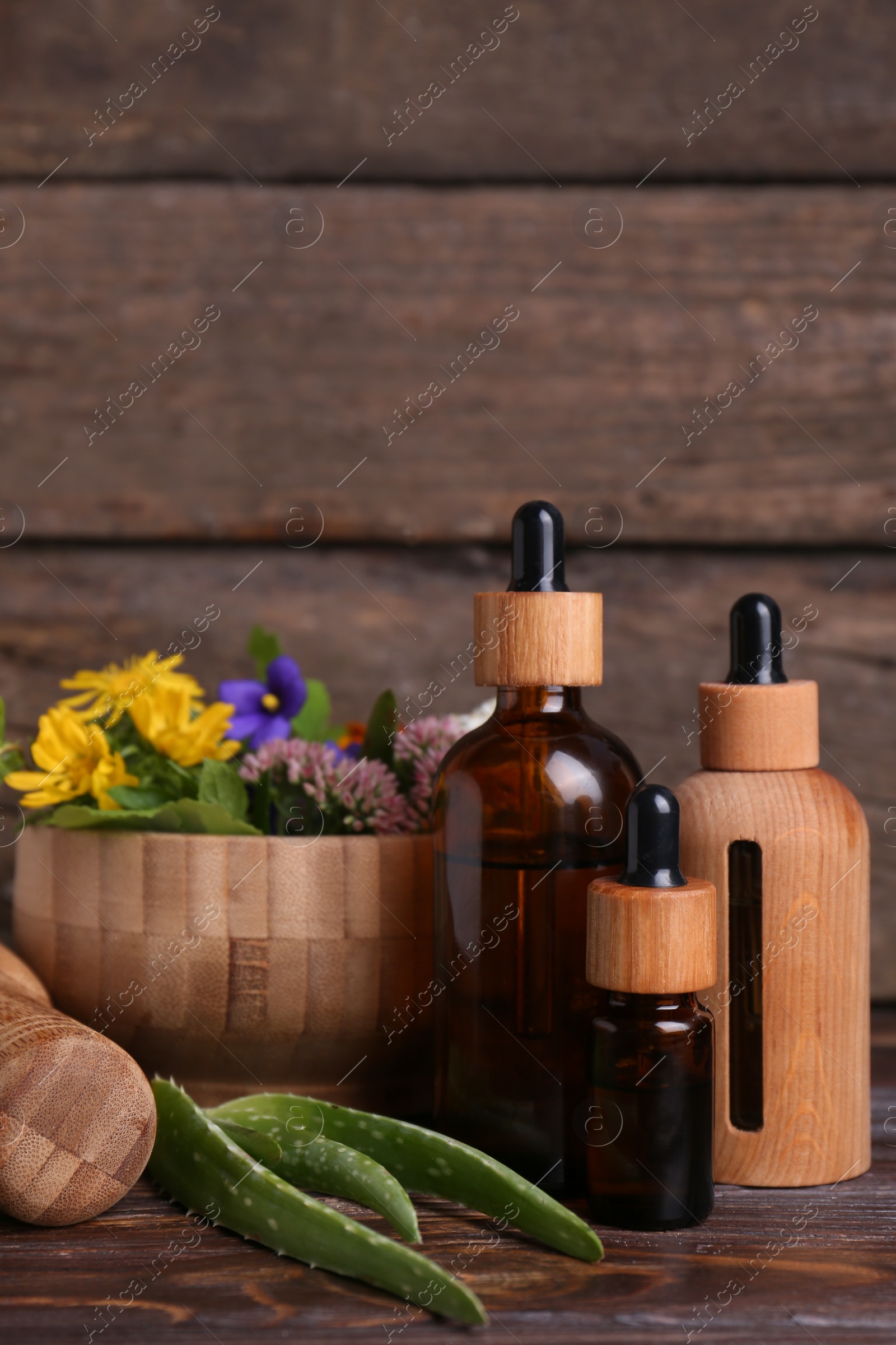 Photo of Glass bottles of aromatic essential oil and mortar with different herbs on wooden table