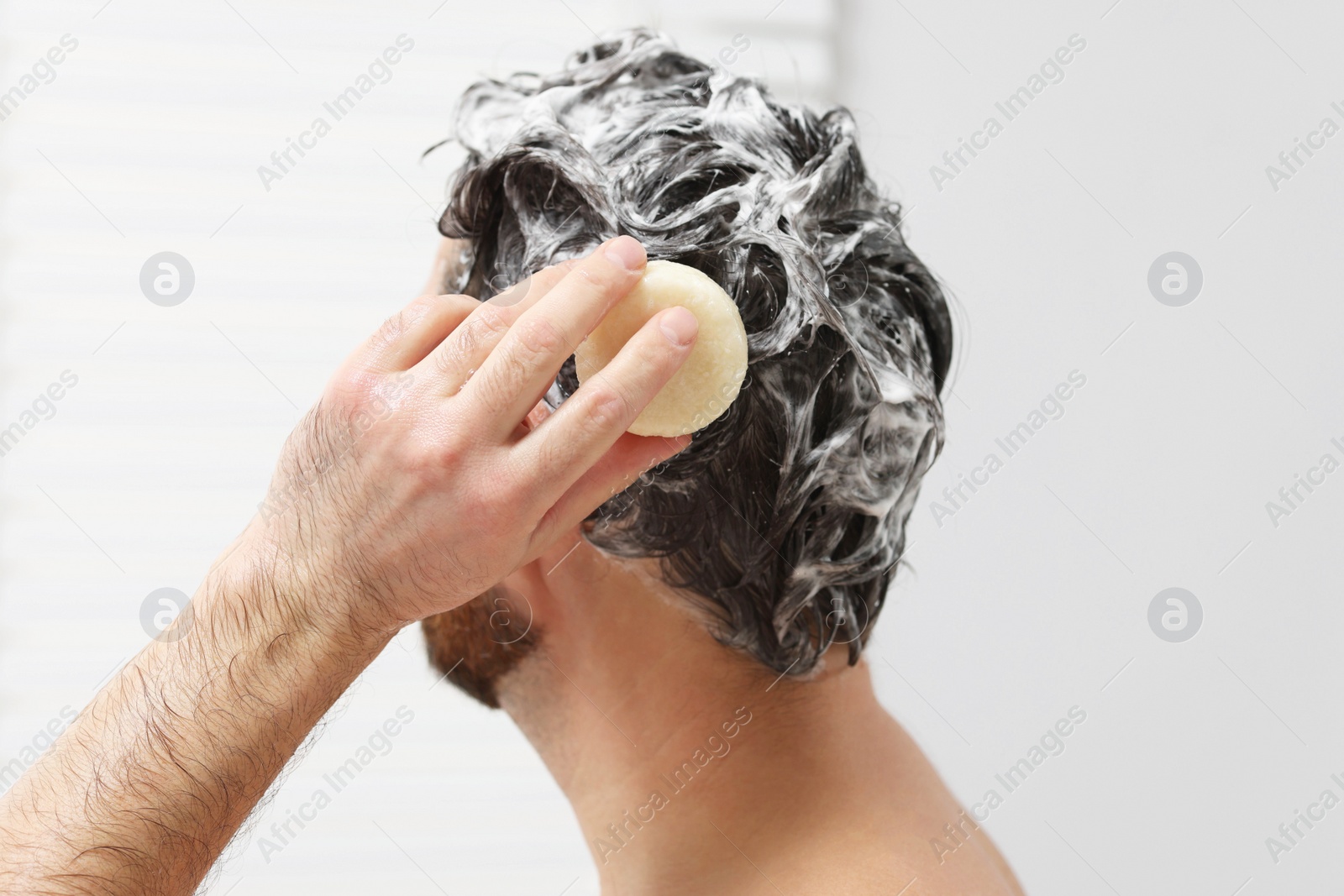 Photo of Man washing his hair with solid shampoo bar in shower, closeup
