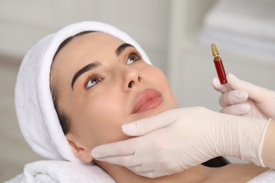 Professional cosmetologist holding skincare ampoule while working with client in clinic, closeup