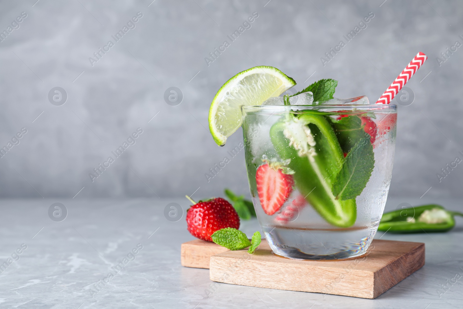 Photo of Spicy cocktail with jalapeno, strawberry, lime and mint on light grey table. Space for text