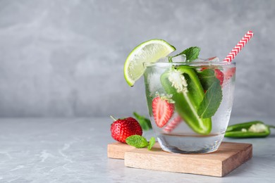 Photo of Spicy cocktail with jalapeno, strawberry, lime and mint on light grey table. Space for text