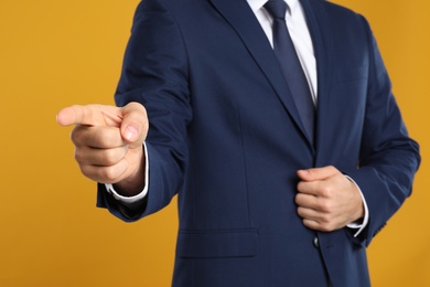 Photo of Businessman touching something on yellow background, closeup. Finger gesture