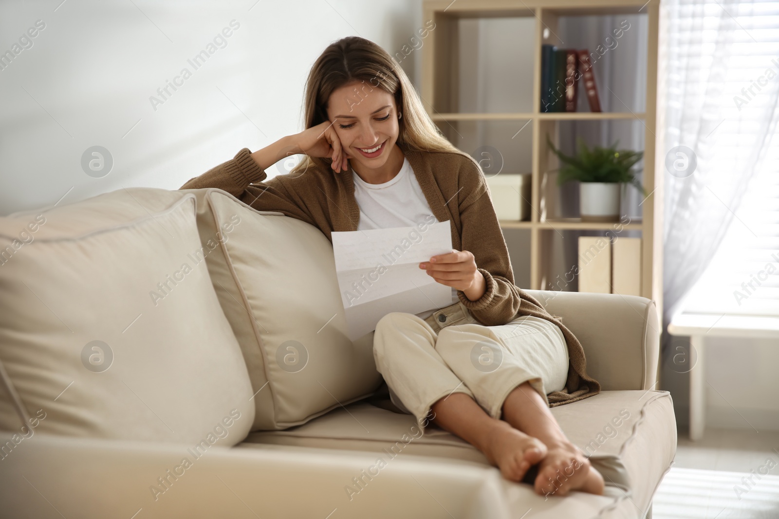 Photo of Happy woman reading letter on sofa at home