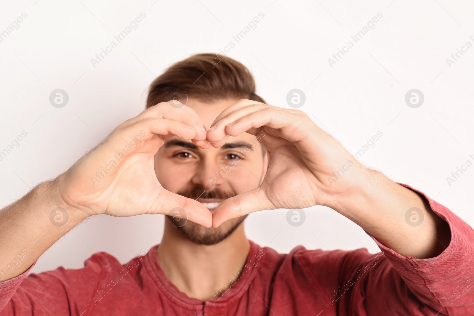 Photo of Man looking through heart made with his hands on white background