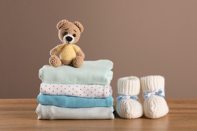 Photo of Stack of baby boy's clothes, booties and toy on wooden table against brown background, space for text