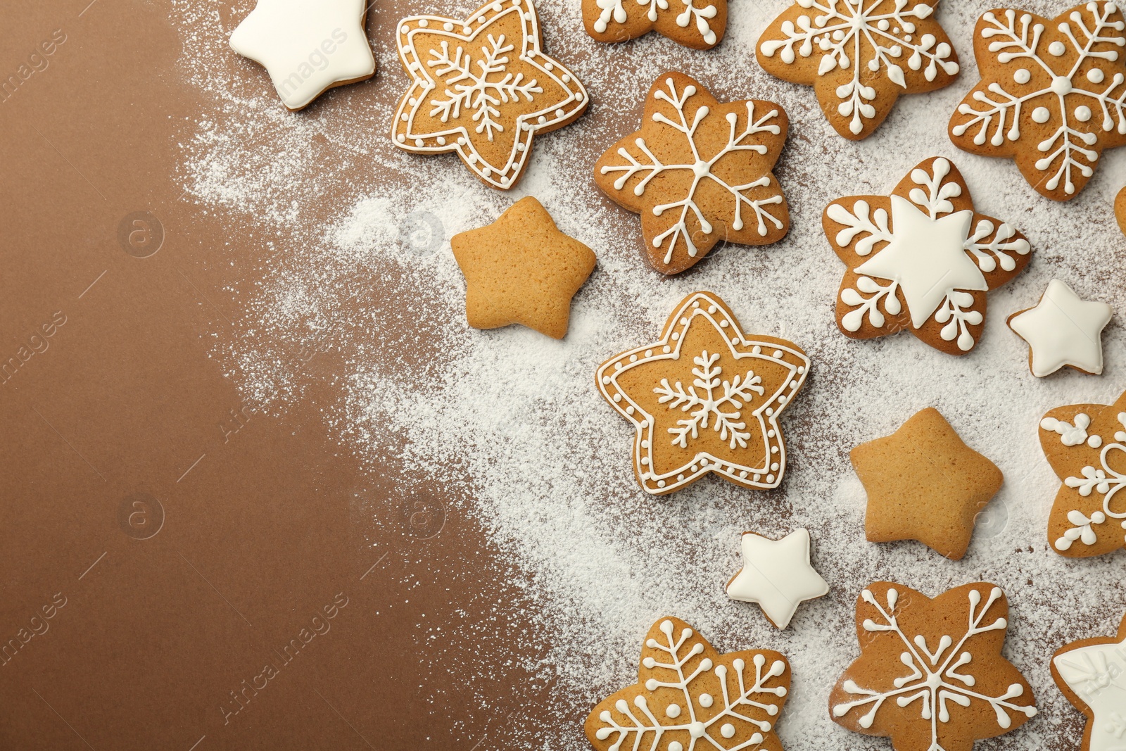 Photo of Tasty Christmas cookies with icing and powdered sugar on brown background, flat lay. Space for text