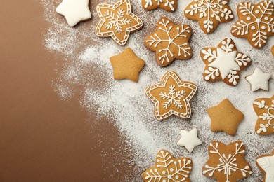 Photo of Tasty Christmas cookies with icing and powdered sugar on brown background, flat lay. Space for text