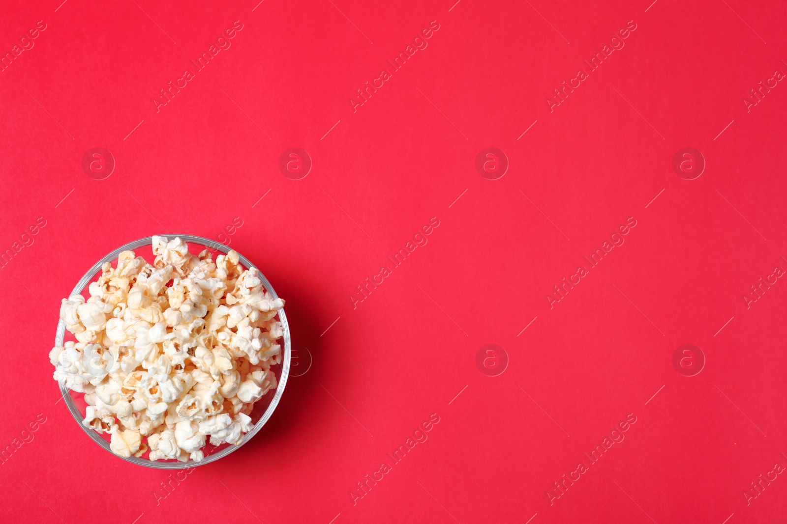 Photo of Glass bowl with tasty popcorn on color background, top view. Space for text