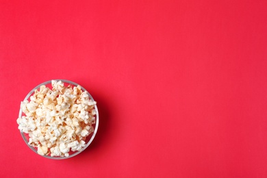 Photo of Glass bowl with tasty popcorn on color background, top view. Space for text