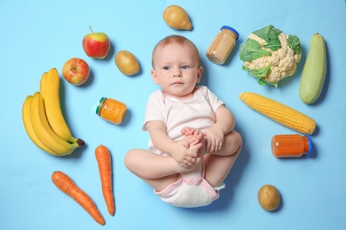 Photo of Cute little child with ingredients and purees in jars on color background, top view. Baby food