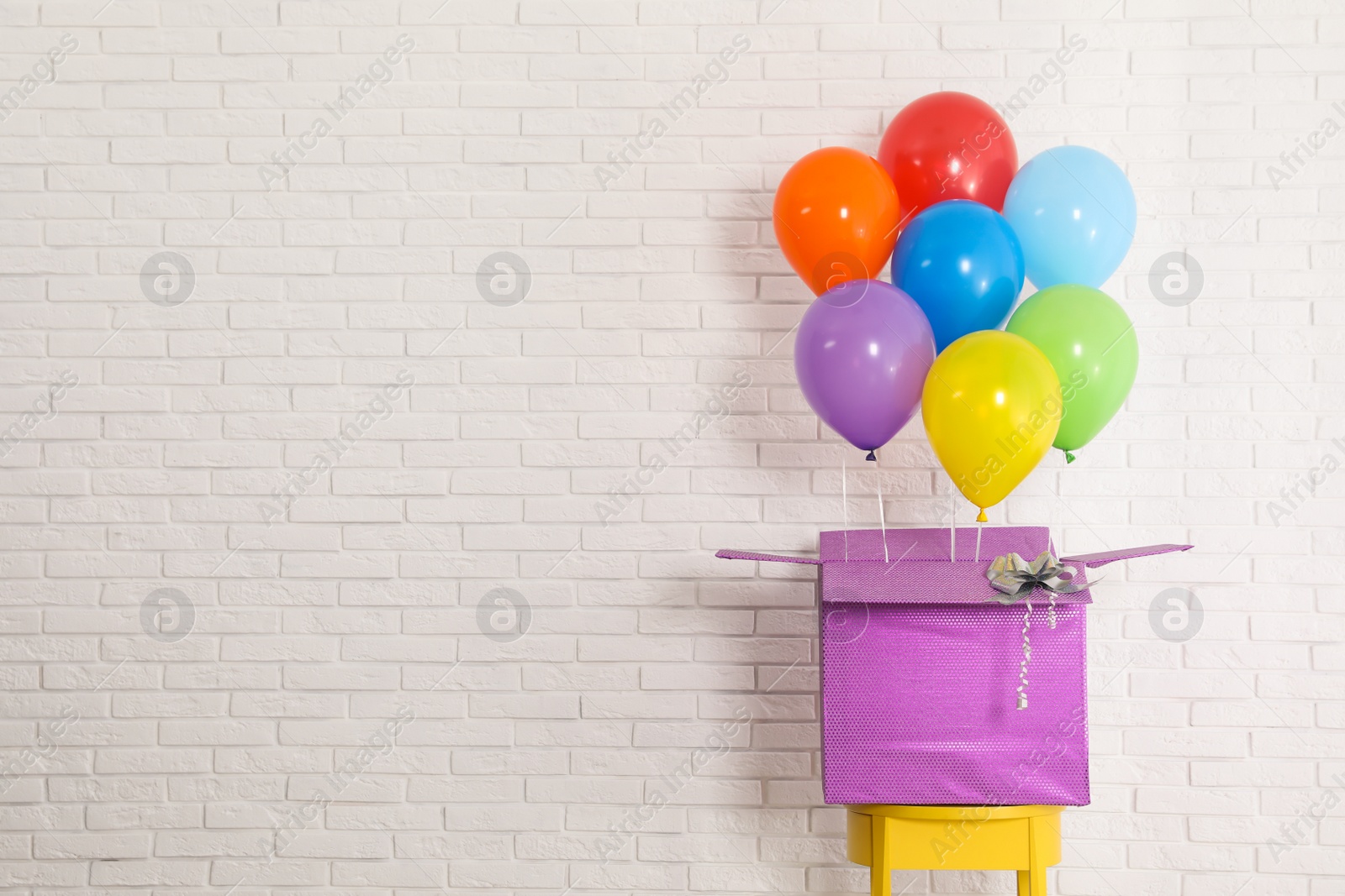 Photo of Gift box with bright air balloons against white brick wall. Space for text