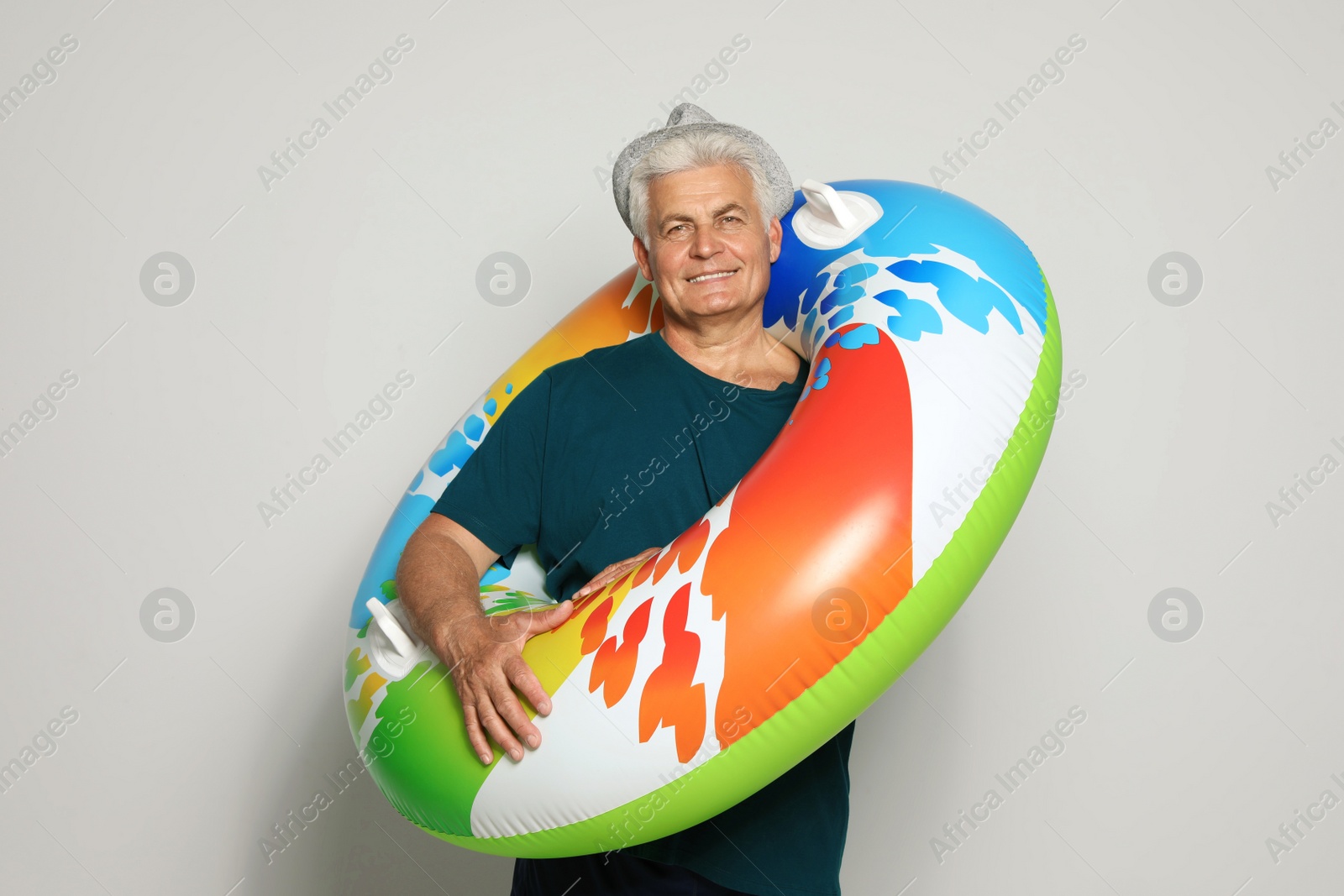 Photo of Funny mature man with bright inflatable ring on light background