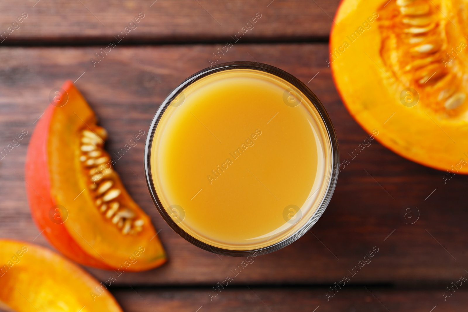 Photo of Tasty pumpkin juice in glass and cut pumpkin on wooden table, flat lay