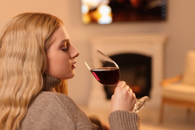 Beautiful young woman with glass of wine resting near fireplace at home