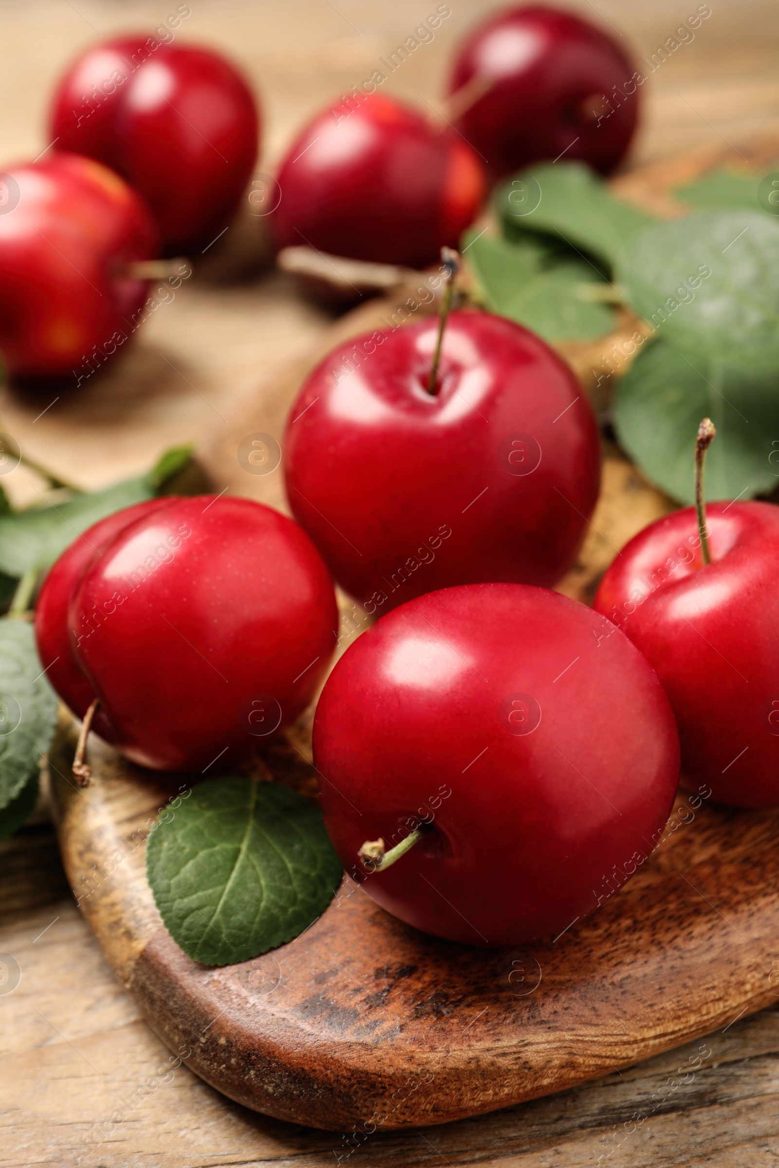 Photo of Delicious ripe cherry plums with leaves on wooden table, closeup