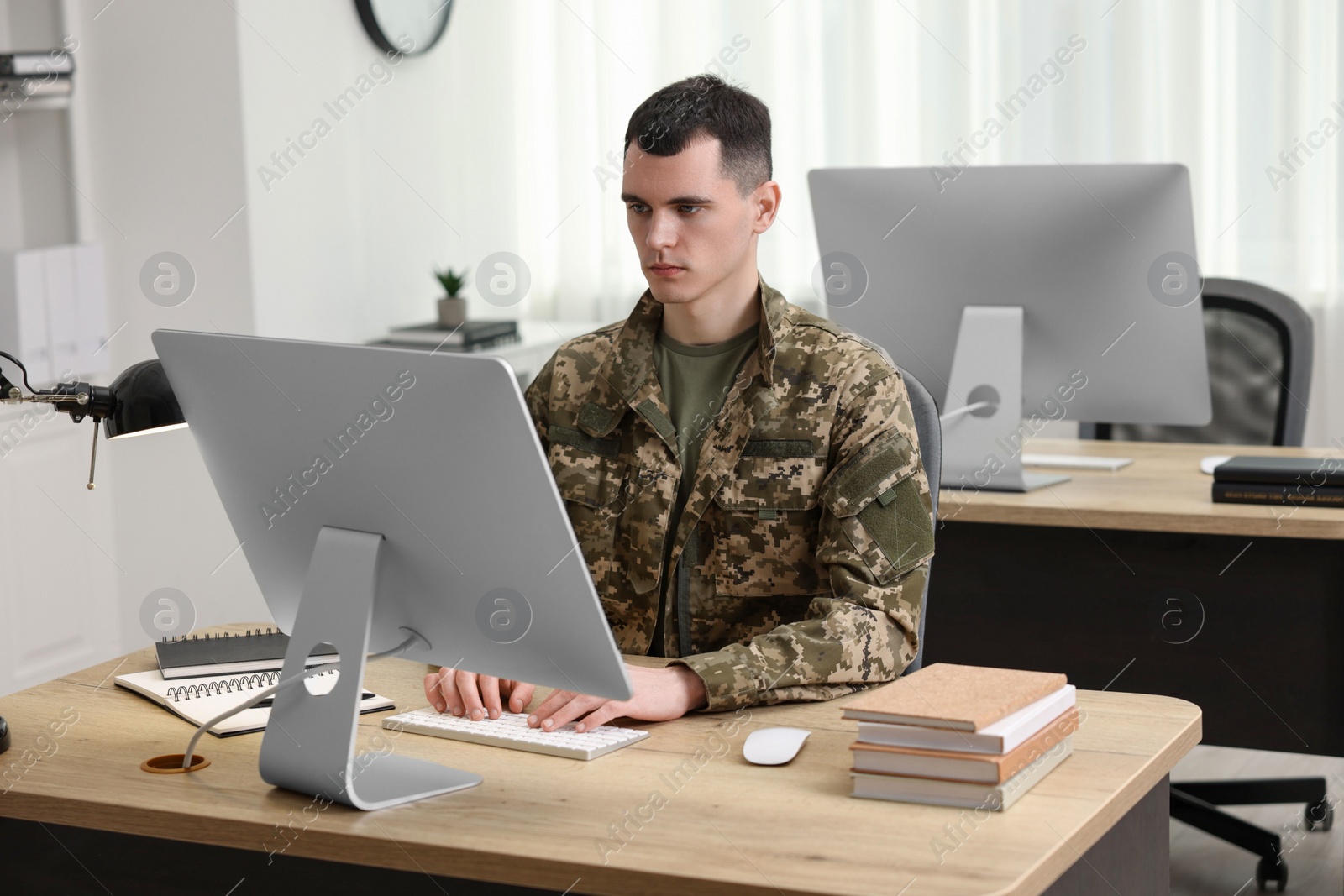 Photo of Military education. Young student in soldier uniform learning at wooden table in room