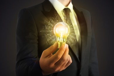 Image of Glow up your ideas. Businessman holding light bulb on dark background, closeup