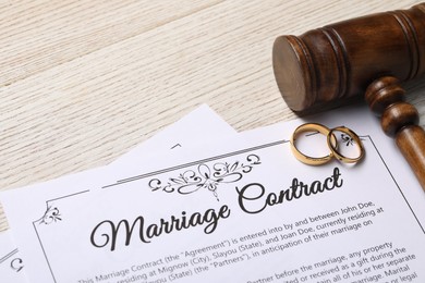 Photo of Marriage contract, golden wedding rings and gavel on wooden table