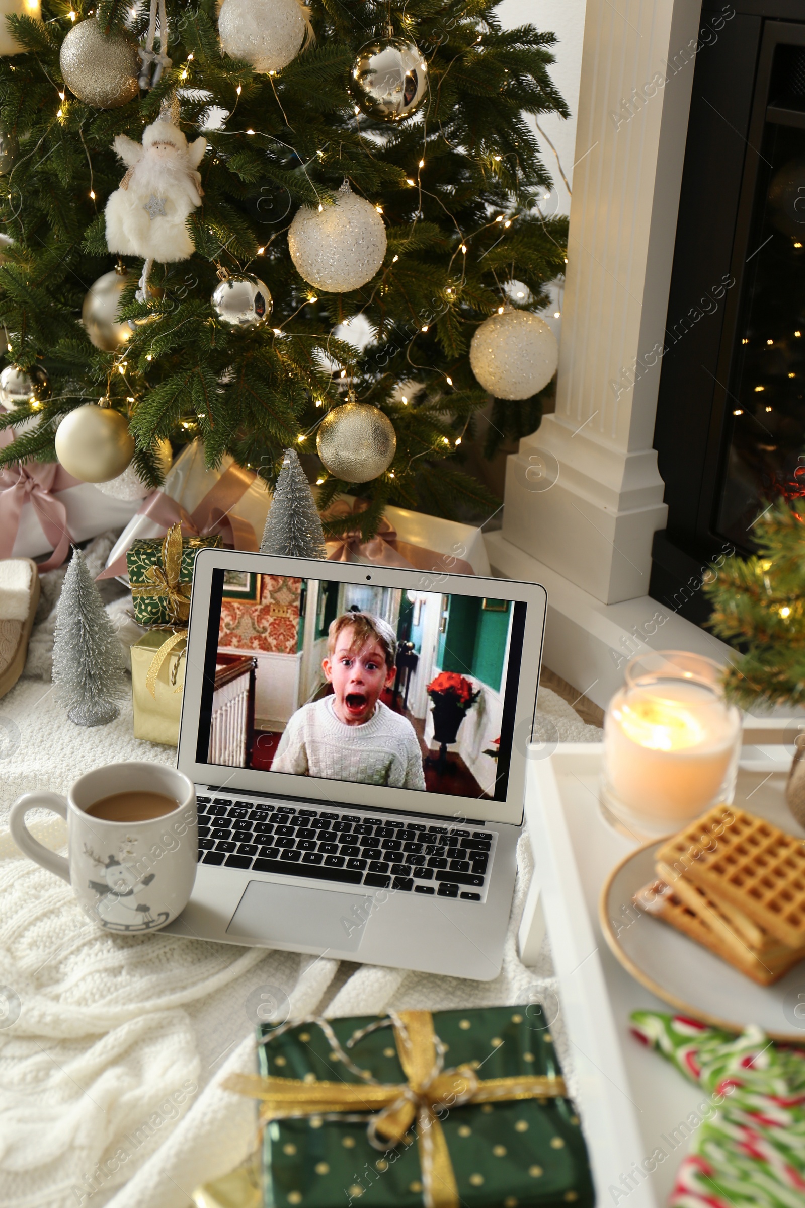 Photo of MYKOLAIV, UKRAINE - DECEMBER 23, 2020: Laptop displaying Home Alone movie near fireplace indoors. Cozy winter holidays atmosphere