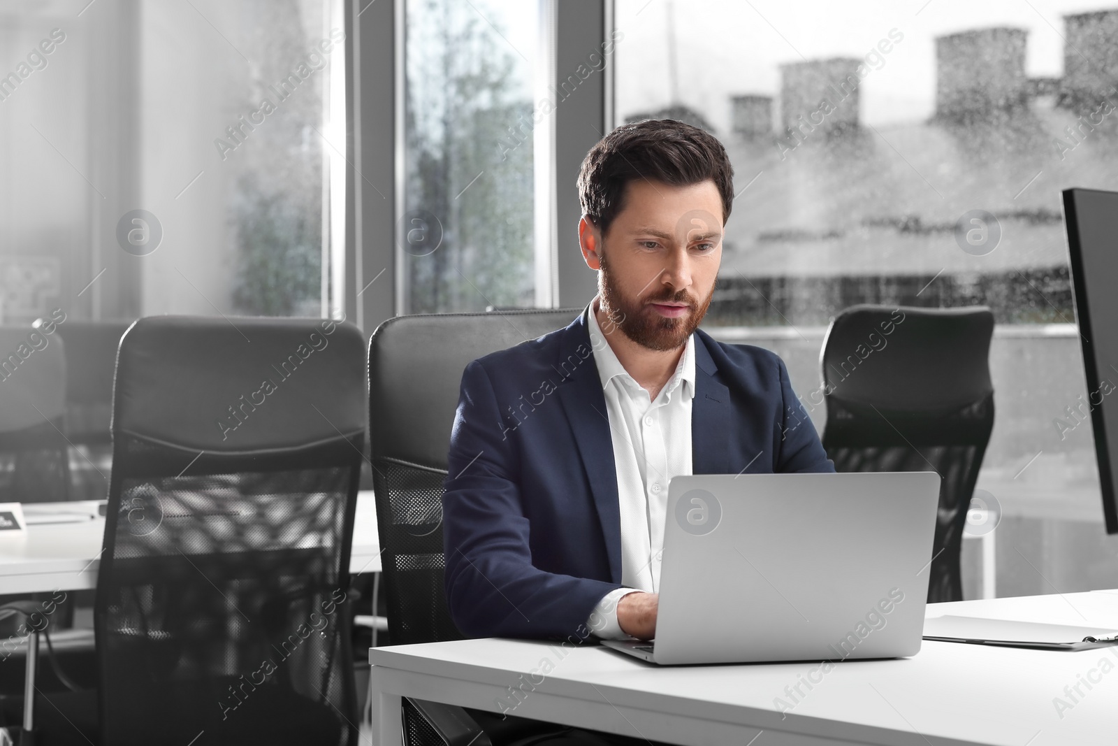 Photo of Man working on laptop at white desk in office. Space for text