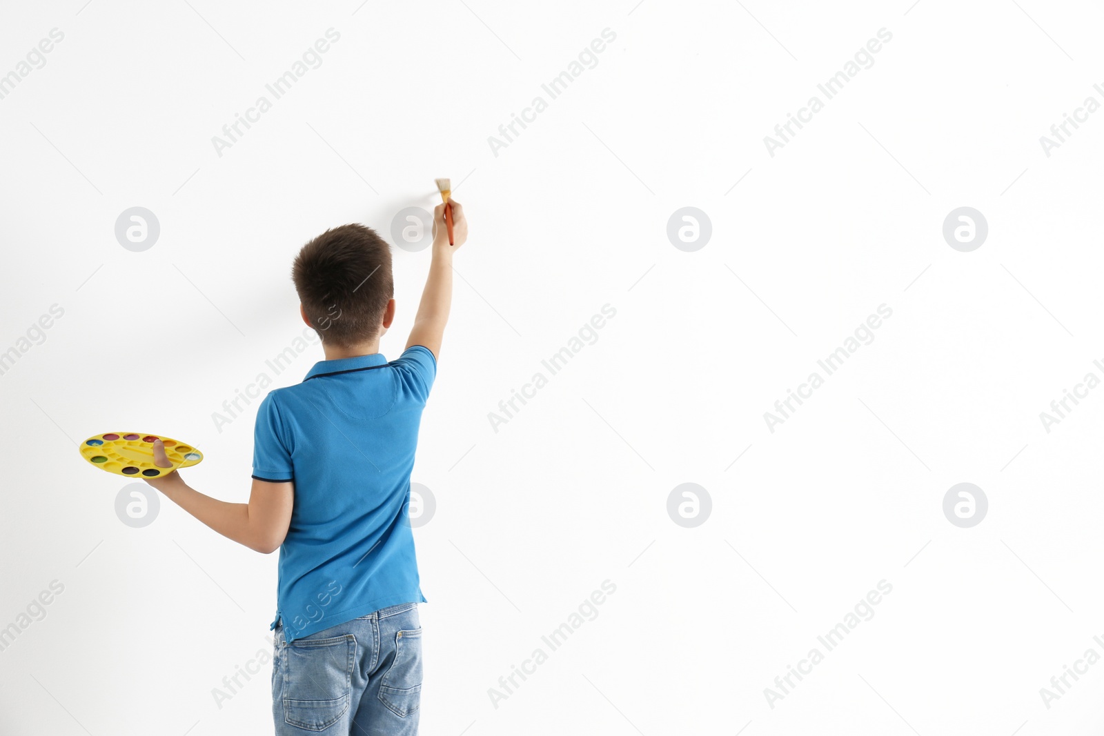 Photo of Little child painting on white wall indoors. Space for text