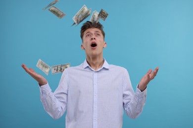 Handsome man under money shower on light blue background