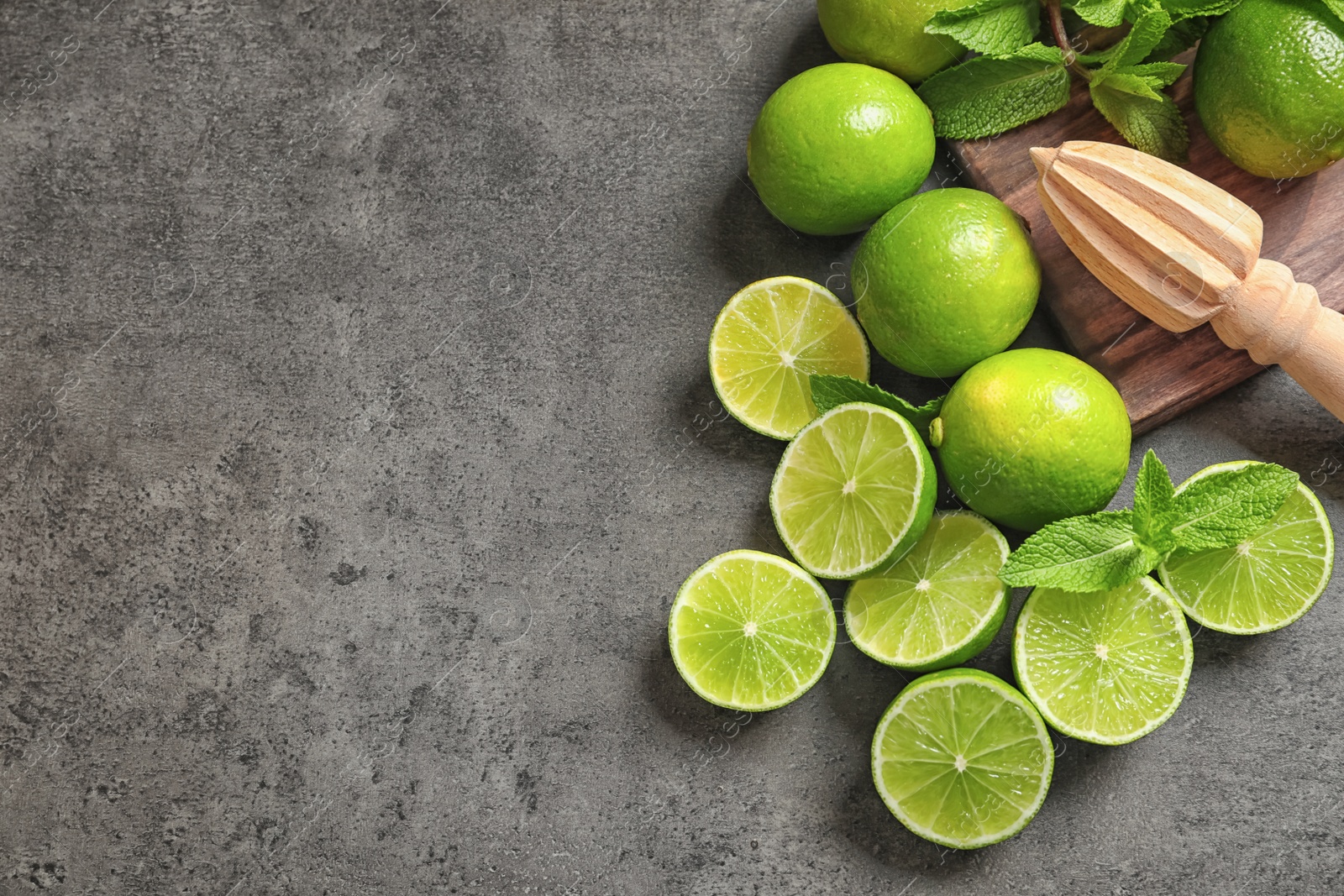 Photo of Flat lay composition with ripe limes, mint and juicer on grey background. Refreshing beverage recipe