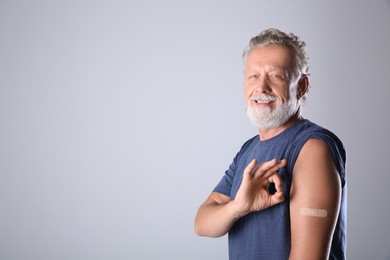 Photo of Cheerful senior man showing arm with bandage after vaccination on grey background. Space for text