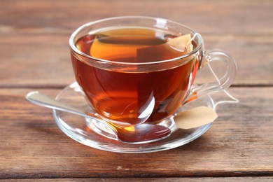 Photo of Brewing aromatic tea. Cup with teabag and spoon on wooden table