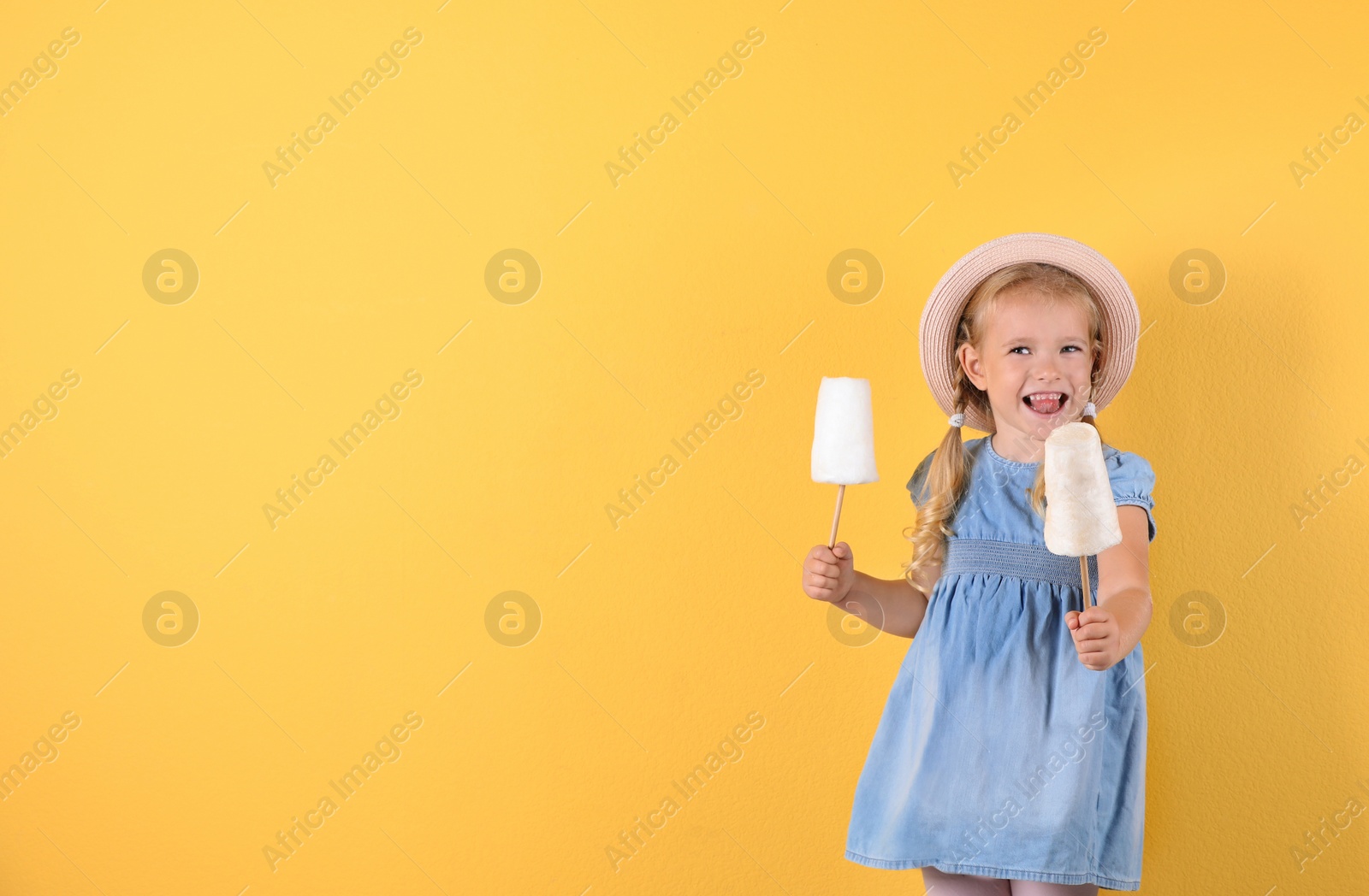 Photo of Cute little girl with cotton candies on color background. Space for text