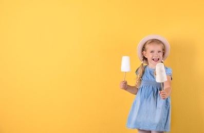 Cute little girl with cotton candies on color background. Space for text