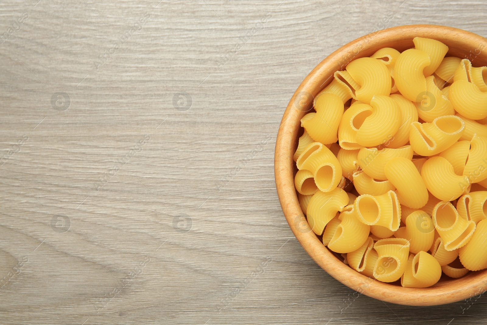 Photo of Raw macaroni pasta in bowl on light grey wooden table, top view. Space for text