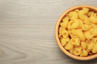 Raw macaroni pasta in bowl on light grey wooden table, top view. Space for text