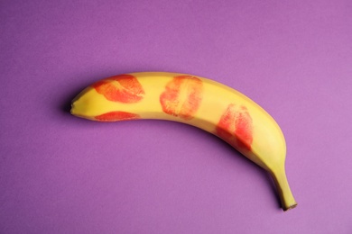 Photo of Fresh banana with red lipstick marks on purple background, top view. Oral sex concept