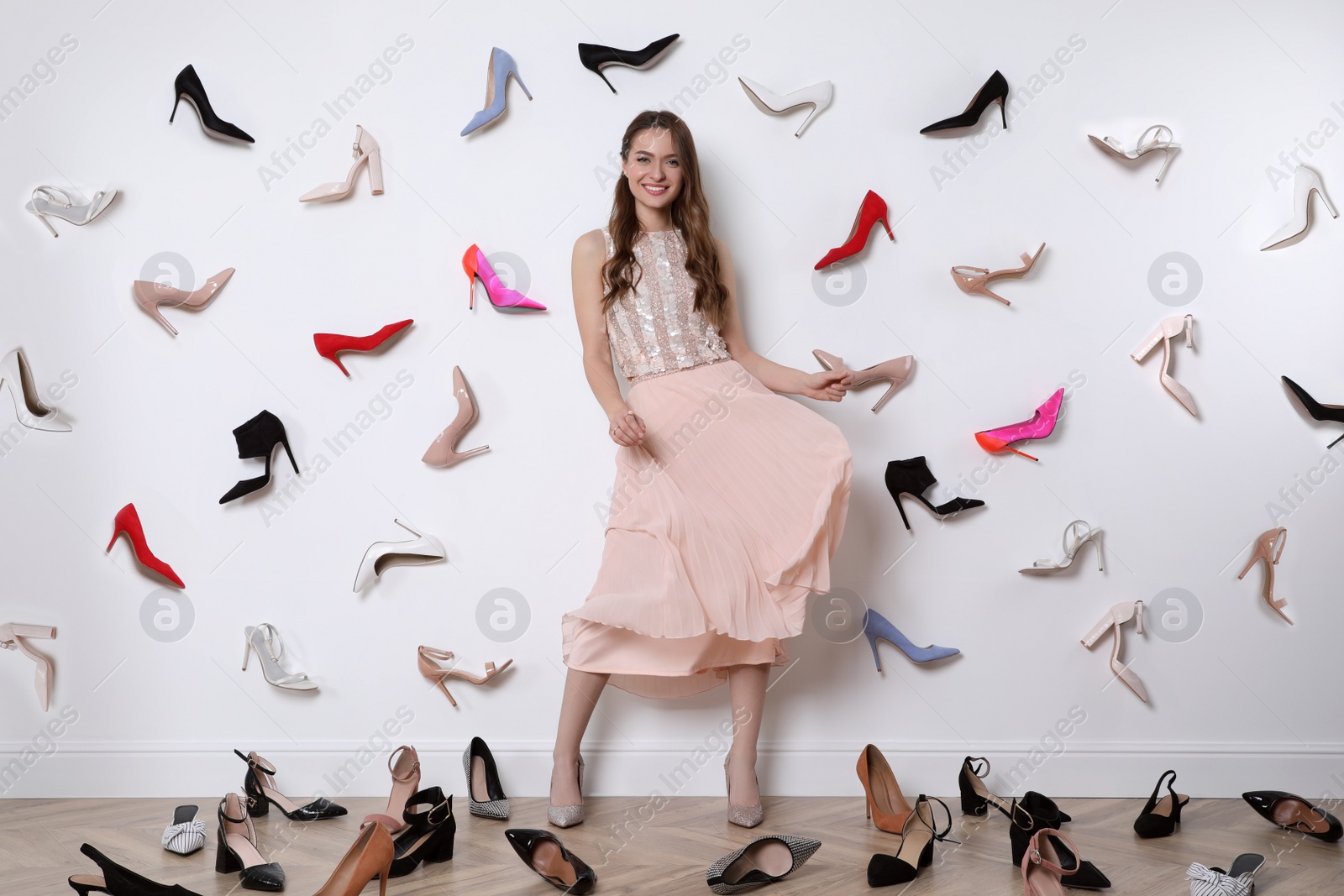 Photo of Fashionable young woman surrounded by many different high heel shoes indoors