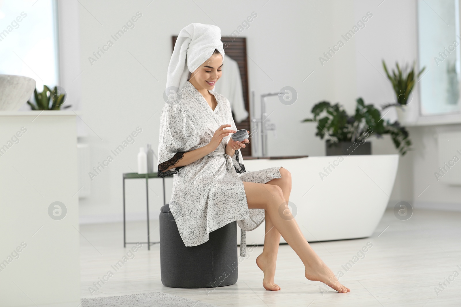 Photo of Beautiful happy woman in stylish bathrobe with jar of cream in bathroom