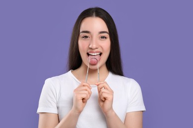 Photo of Happy woman brushing her tongue with cleaner on violet background