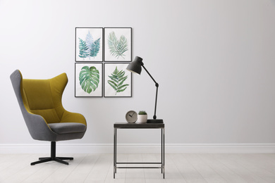 Stylish room interior with comfortable armchair and paintings of tropical leaves. Space for text