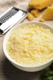 Photo of Delicious grated parmesan cheese in bowl on white wooden table, closeup