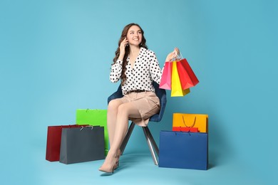 Photo of Happy woman holding colorful shopping bags on armchair against light blue background