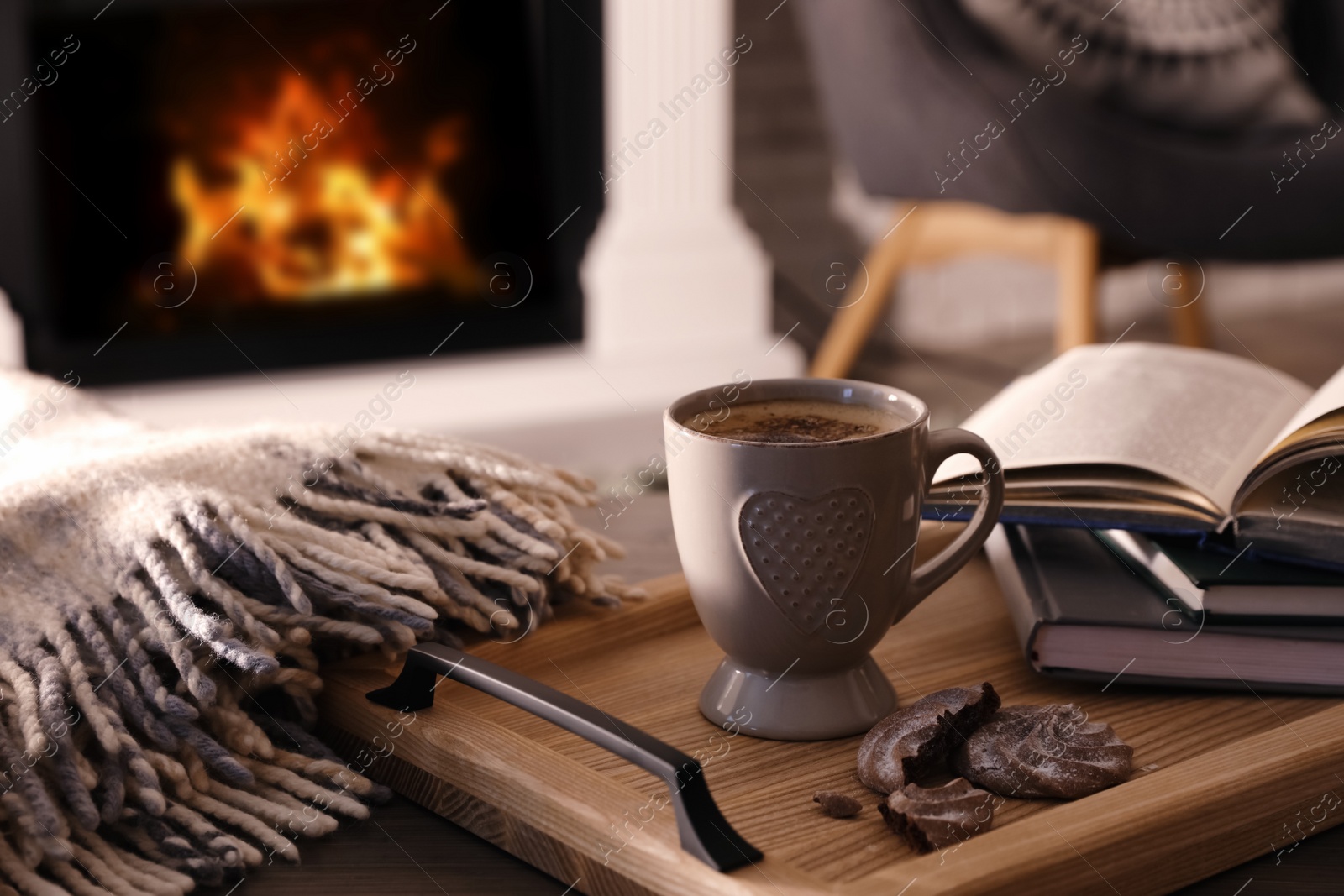 Photo of Cup of coffee, broken cookie and books on wooden table near fireplace indoors. Cozy atmosphere