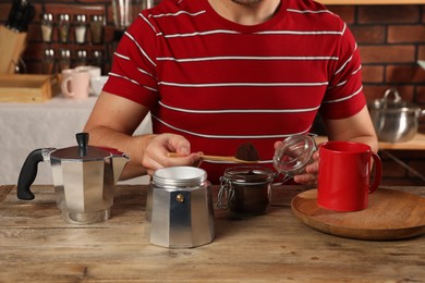 Man putting ground coffee into moka pot at wooden table in kitchen, closeup