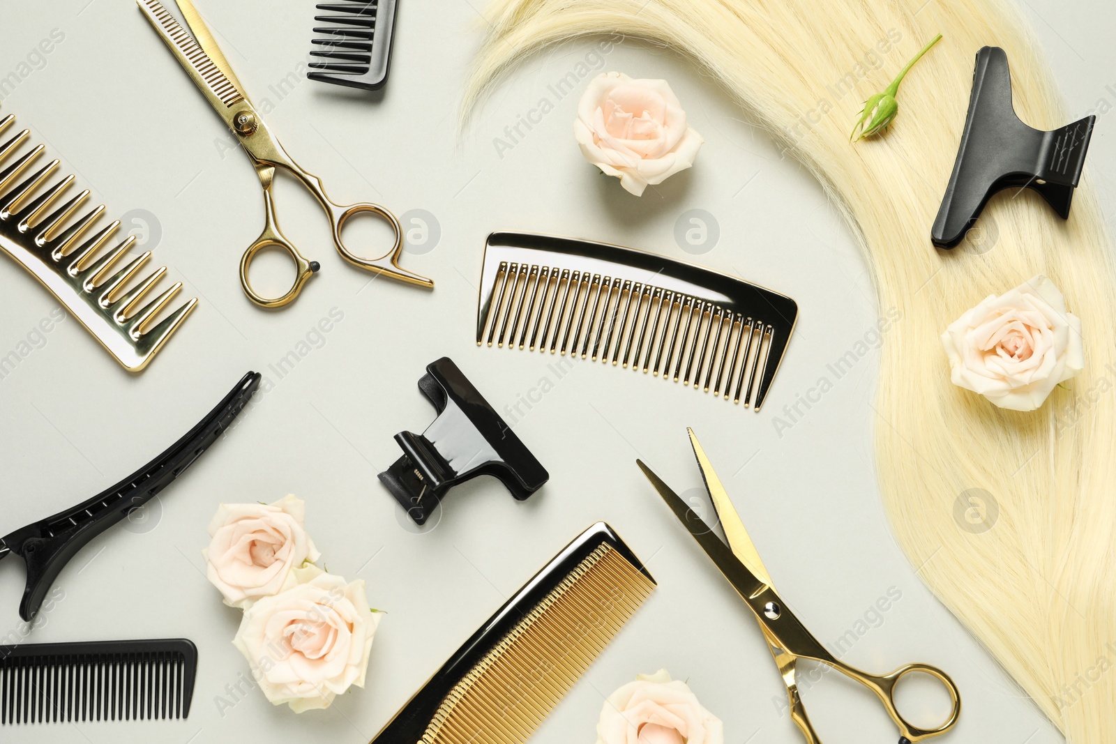 Photo of Flat lay composition with professional hairdresser tools, flowers and blonde hair strand on light grey background